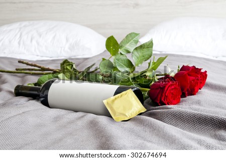 Bottle of wine, red roses and condom on bed - sexy set up