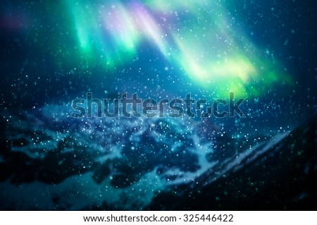 Snow falling against aurora borealis - focus on snowflakes, northern lights and mountains in the background