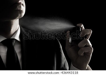 Elegant man in suit and tie using cologne or perfume isolated on black