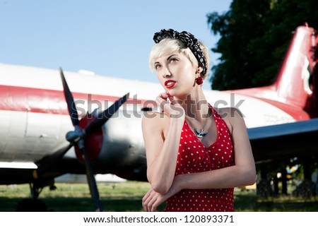 outdoors pin-up portrait of young blond thoughtful caucasian woman in red retro dress.