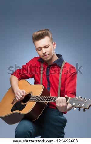 caucasian young vintage man in red shirt playing guitar over blue background