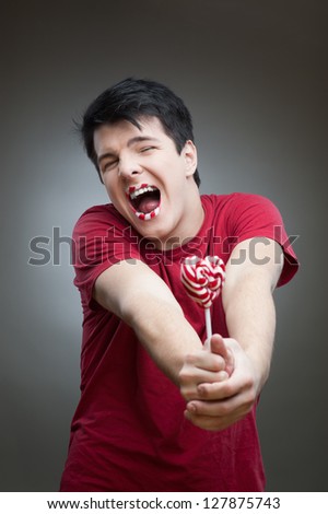 young funny caucasian brunette man in red t-shirt holding lollipop with open mouth