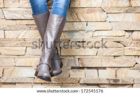 female legs in long brown leather boots sitting at brick wall