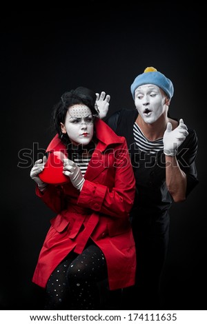 two funny mimes holding red heart isolated on black background