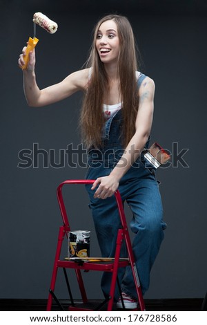 attractive caucasian smiling young woman standing at ladder and holding paint roll