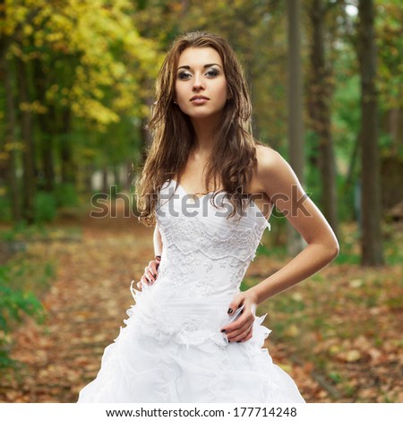outdoors portrait of beautiful young caucasian brunette woman in white wedding dress over green foliage on background