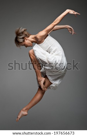 beautiful young caucasian female dancer jumping  over gray background