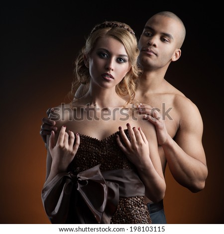 young sensual caucasian woman in dress made of coffee beans and black man standing over gradient orange background