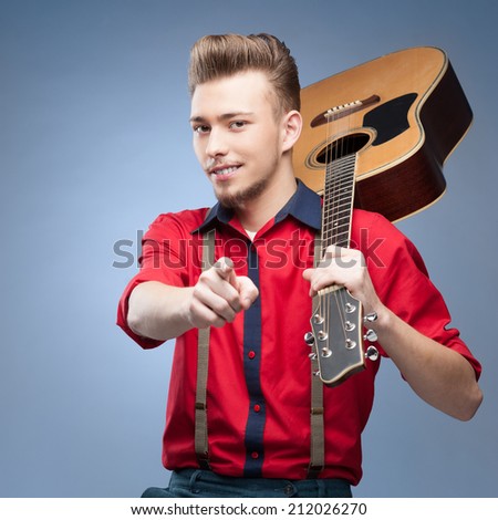 caucasian  young smiling vintage man in red shirt holding guitar over blue background