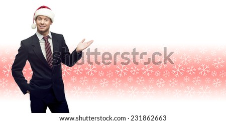 smiling young business man in santa hat showing empty space over winter snowflakes background