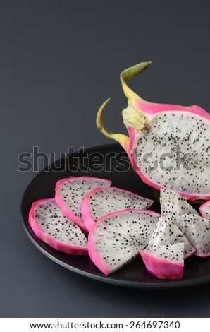 dragon fruit cut into pieces, in a black plate on a black background, vertical