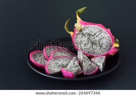 dragon fruit cut into pieces, in a black plate on a black background