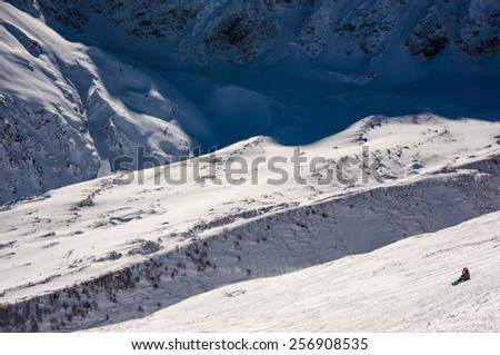 little figure of snowboarder sitting on the slope and watching on huge mountains at Russia, Caucasus