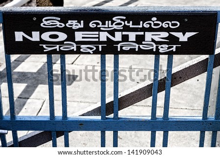 a wooden sign affixed above a wooden gate shows in English and Asian language the prohibition of entry to a path