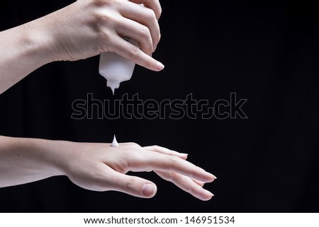 Female hands, isolated on black background, are smearing cream on themselves