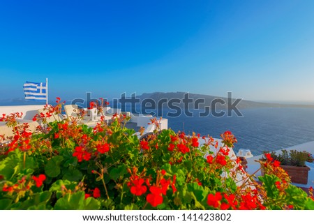 Greece Santorini island in Cyclades, Greek flag waving above colorful flowers above the sea of caldera