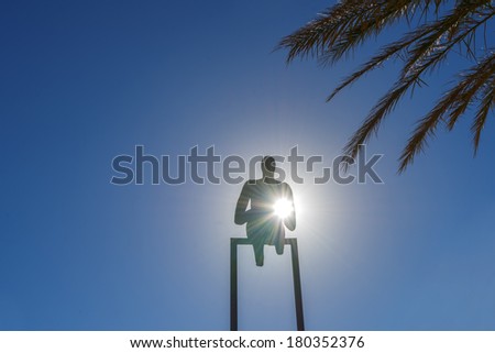 Statue of a man raising his hand with sun background