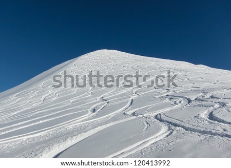 View on a snow-covered summit with wavy snow tracks of skiers and snowboarders