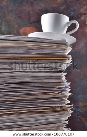 Cup on a pile of papers against the background of old wooden board