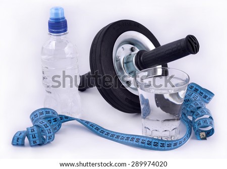 Bottle of water, glass of water, roller wheel for abdominals and measuring tape on white