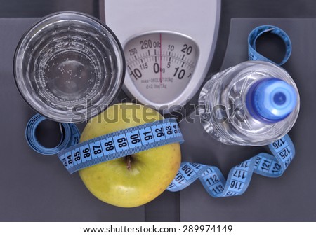 Bottle of water, green apple, glass of water and measuring tape on a scale