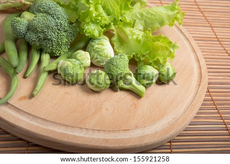 Fresh raw asparagus beans, brussels sprouts, broccoli and lettuce on  wooden board.