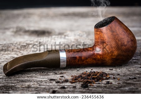 tobacco pipe from briar with smoke in wooden grey table.