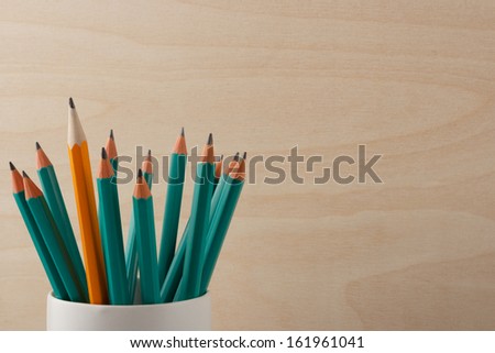 an orange lead pencil among green ones against a wooden board