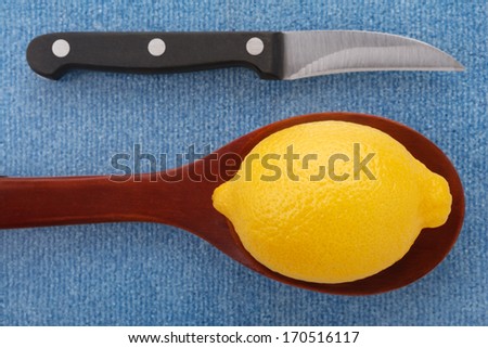 a fresh bright yellow lemon in a wooden spoon next to a carving knife