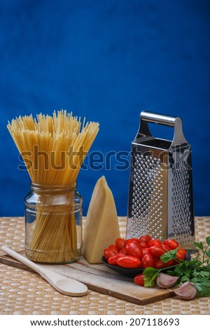 cheese, grater, spaghetti, tomatoes, parsley and garlic on a kitchen table