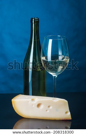 an open bottle of white wine with a glass and a piece of cheese