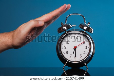 a vintage alarm clock on blue background and a human hand which is about to stop it