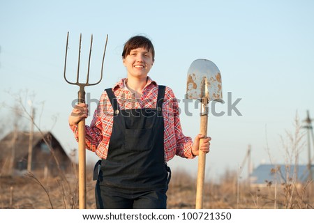 Happy female farmer  with spade and pitchfork in field