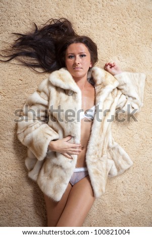 Sexy woman in fur coat laying over  rug