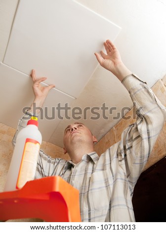 Man glues ceiling tile at home