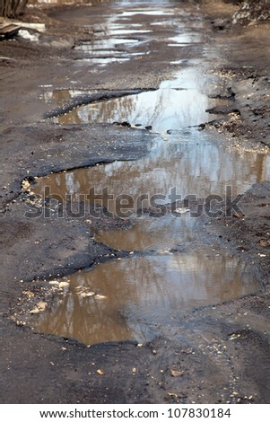 after winter a tarmac road has a large, deep, water filled potholes
