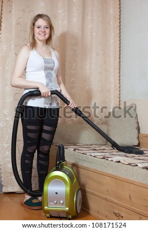 Woman cleans with vacuum cleaner in living room