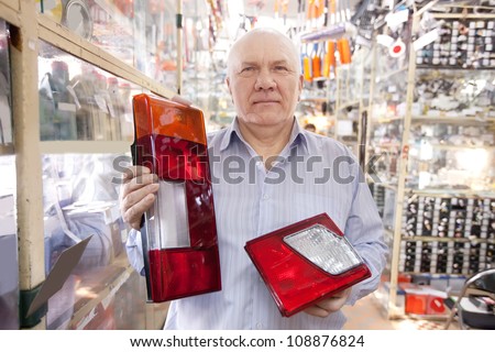 mature man holds  automotive  headlight  in  auto parts store