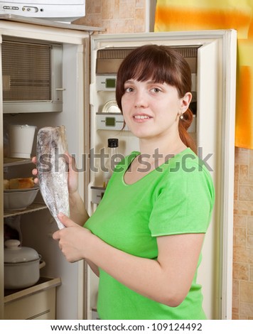 Young woman putting fresh frozen fish into refrigerator  at home