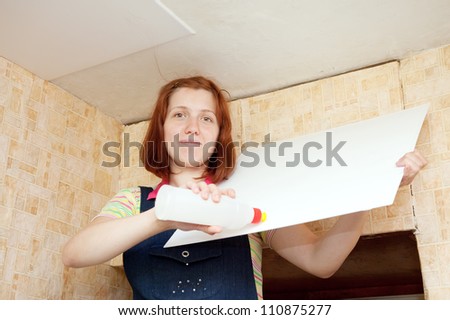 Young woman glues ceiling tile at home