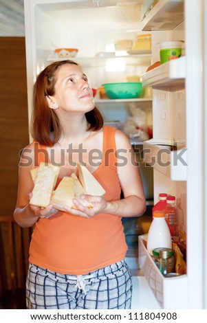 pregnant woman  with cheese near fridge at home