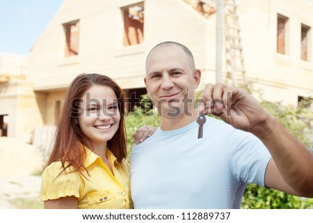 Happy couple with key against building new brick house