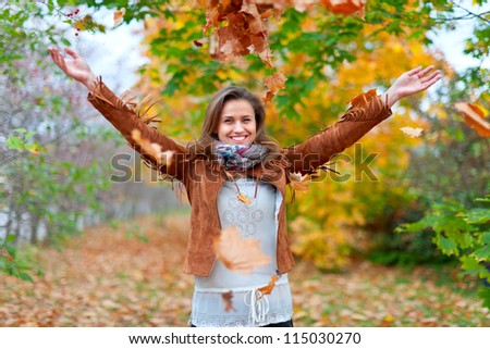 Happy girl throws maple leaves in autumn park