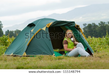 Happy female tourist drinking tea in front camp tent