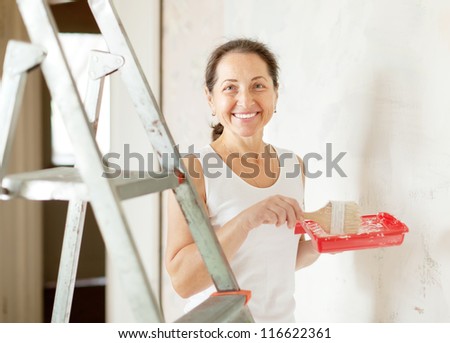 Happy mature woman paints wall with brush at home