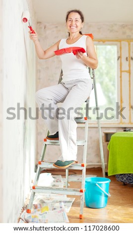 Happy woman paints wall with roller at home
