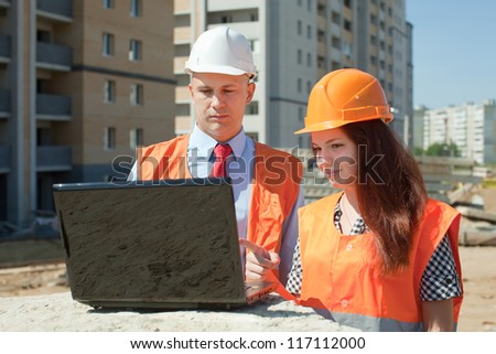 Two architects wearing protective helmet works in front of building site