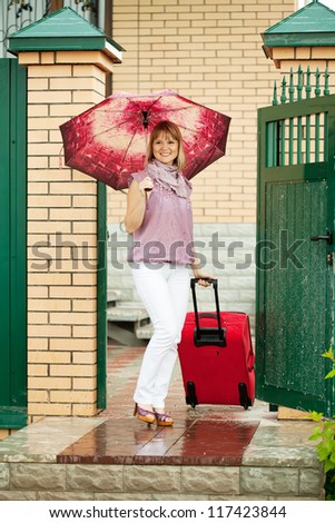 Happy woman with luggage standing near home door