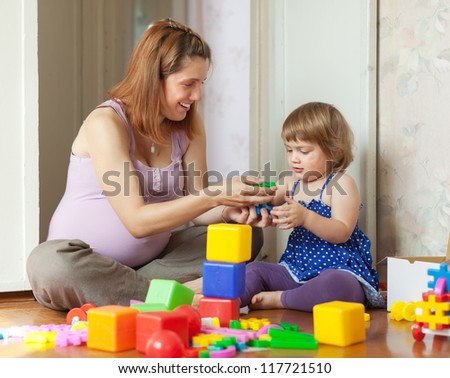 Happy pregnant mother plays with child in home interior