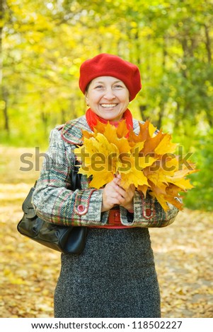elderly woman with maple leaves walking in autumn park